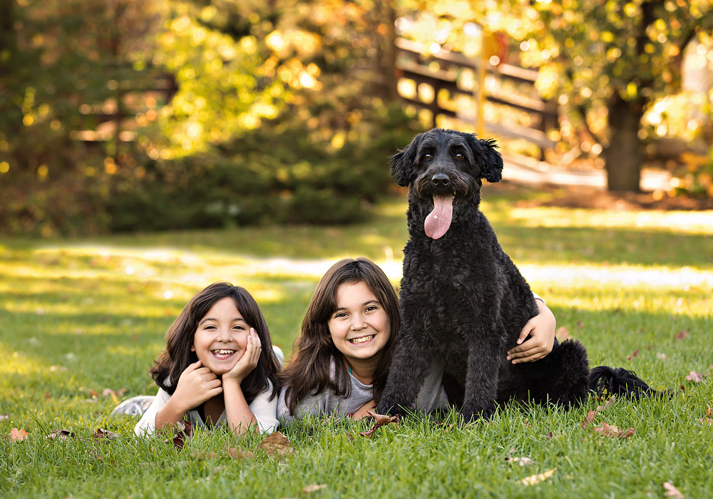 two girls and their black standard poodle in park